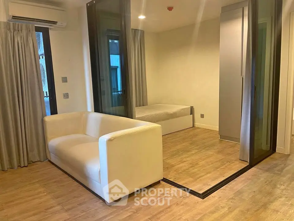 Modern studio apartment with glass partition and cozy sofa, featuring wooden flooring and neutral tones.