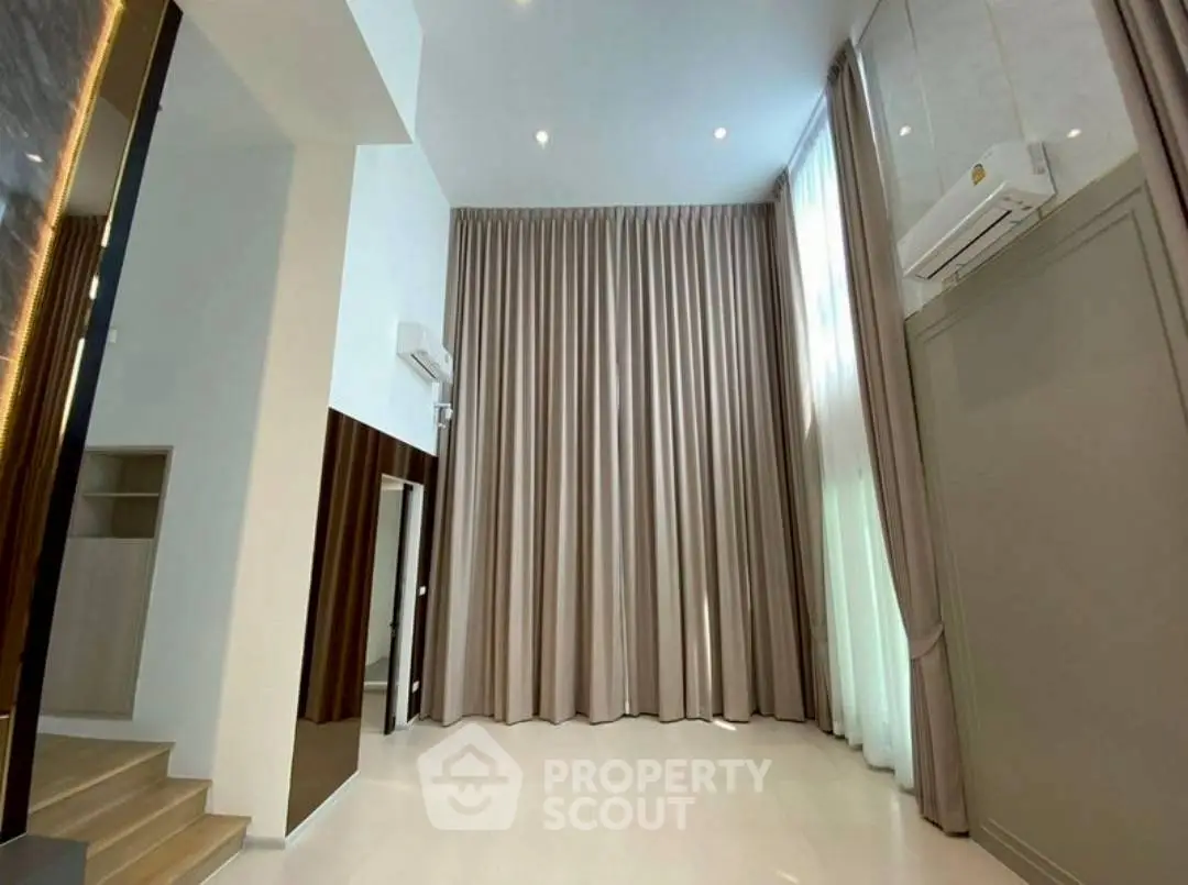 Spacious high-ceiling living room with elegant curtains and modern air conditioning.