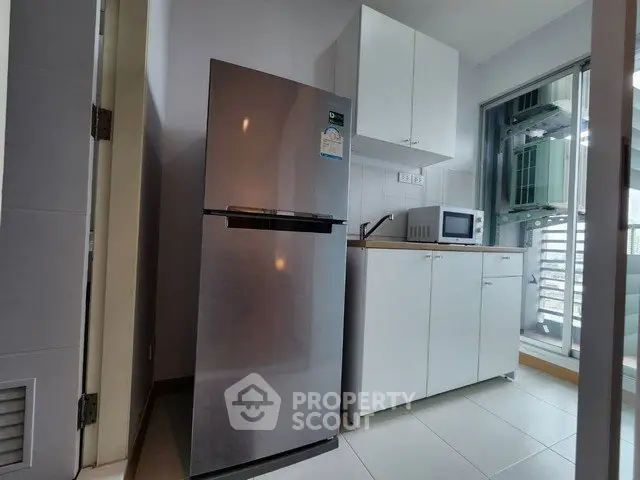Modern kitchen with stainless steel fridge and microwave, featuring sleek cabinetry and balcony access.