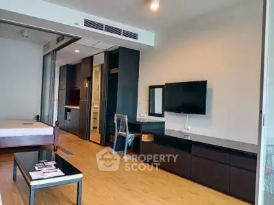 Modern studio apartment with sleek furnishings and open layout, featuring a wall-mounted TV and wooden flooring.