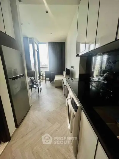 Modern kitchen with sleek appliances and open layout leading to a bright living area with large windows.