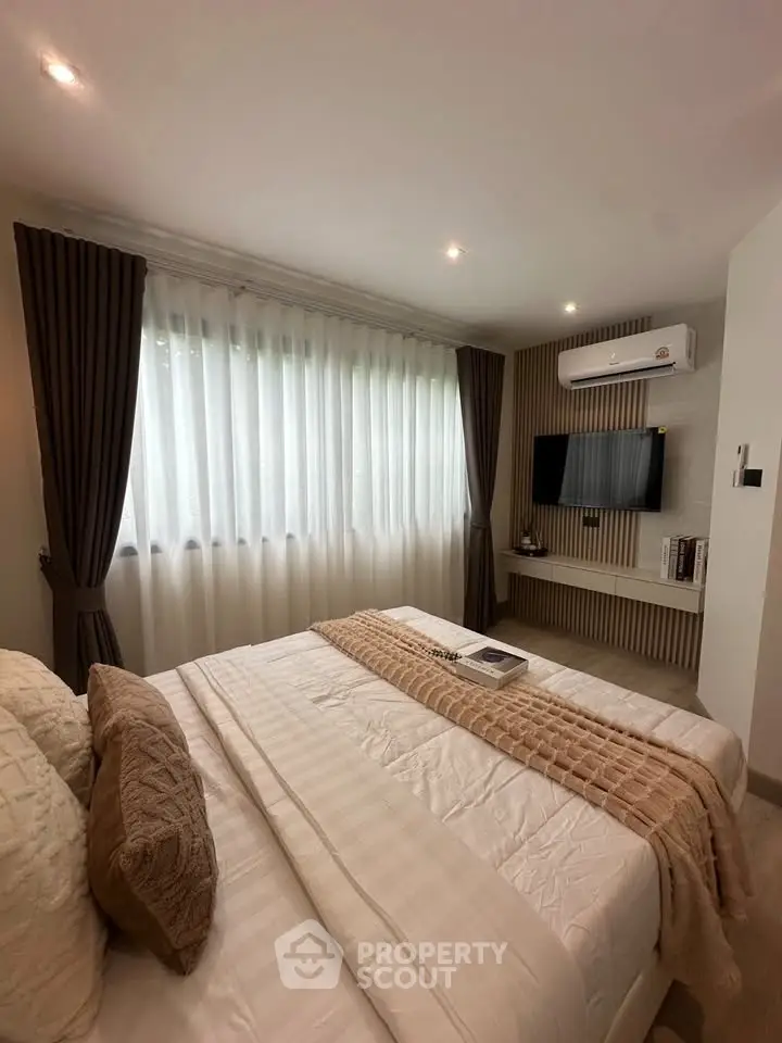 Cozy bedroom with modern decor, featuring a comfortable bed, wall-mounted TV, and large window with curtains.