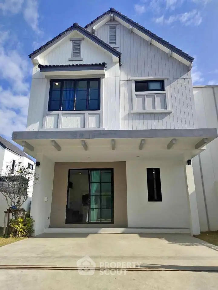 Modern two-story house with white facade and large windows under clear blue sky.