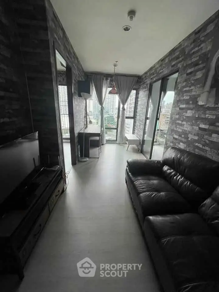 Modern living room with city view, featuring dark leather sofa and sleek decor.