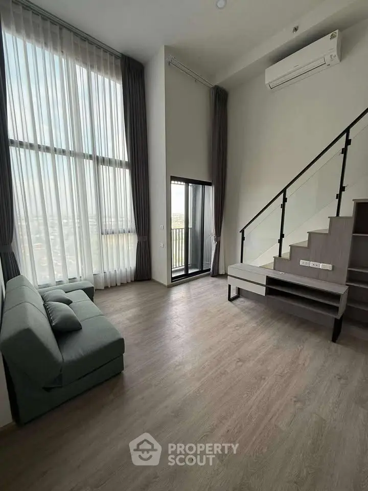 Modern loft apartment with high ceilings and large windows, featuring a sleek staircase and cozy seating area.