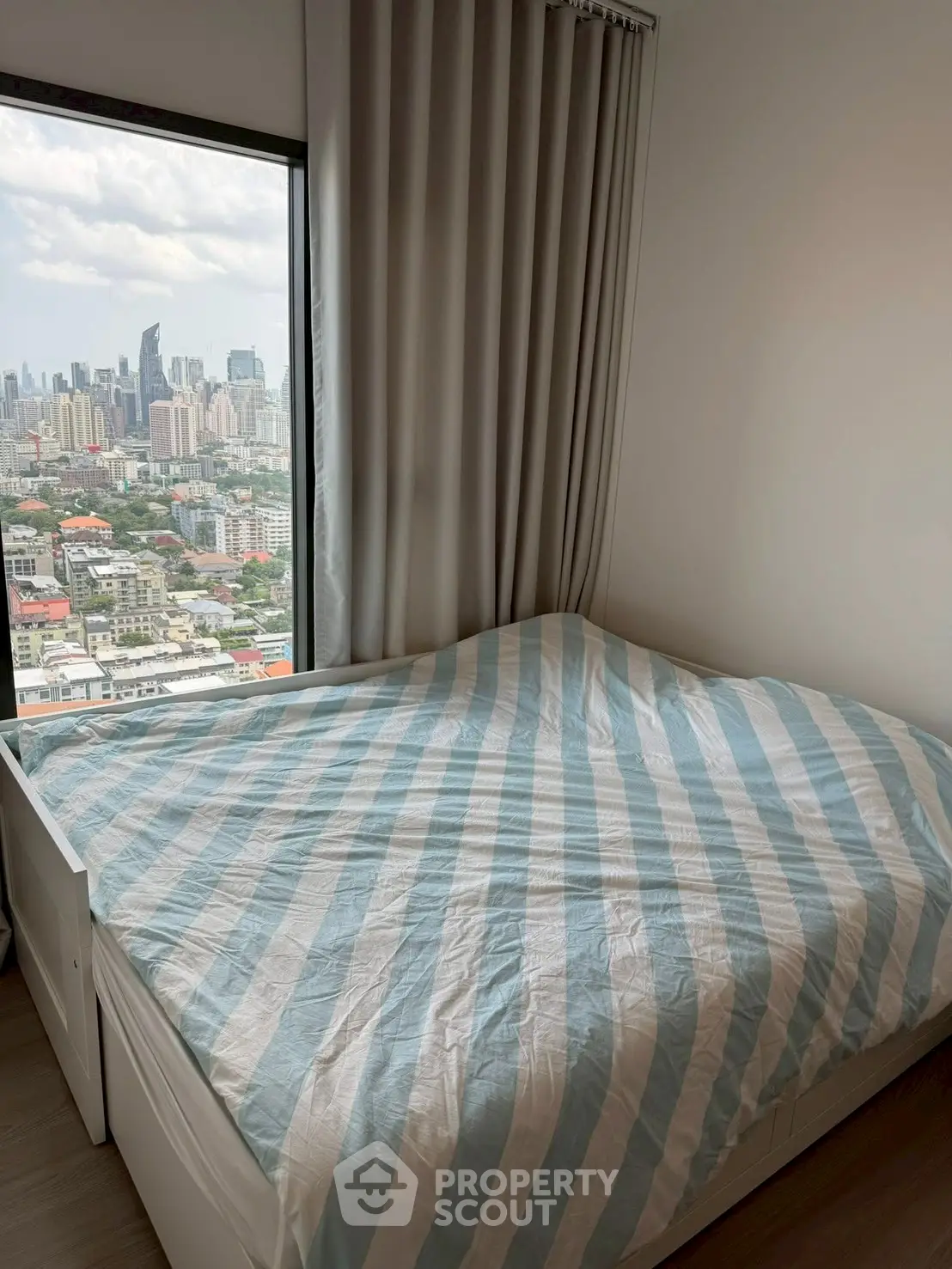 Cozy bedroom with city view, featuring a comfortable bed and large window for natural light.