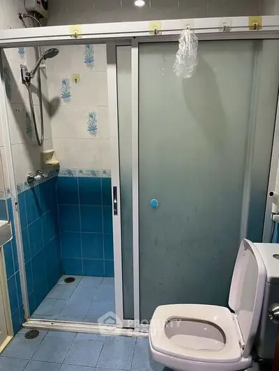 Compact bathroom with blue tiles and sliding shower door, featuring a toilet and showerhead.