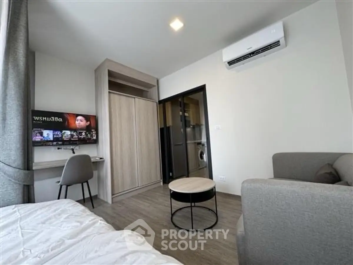 Modern studio apartment with cozy living area and wall-mounted TV, featuring sleek furniture and air conditioning.