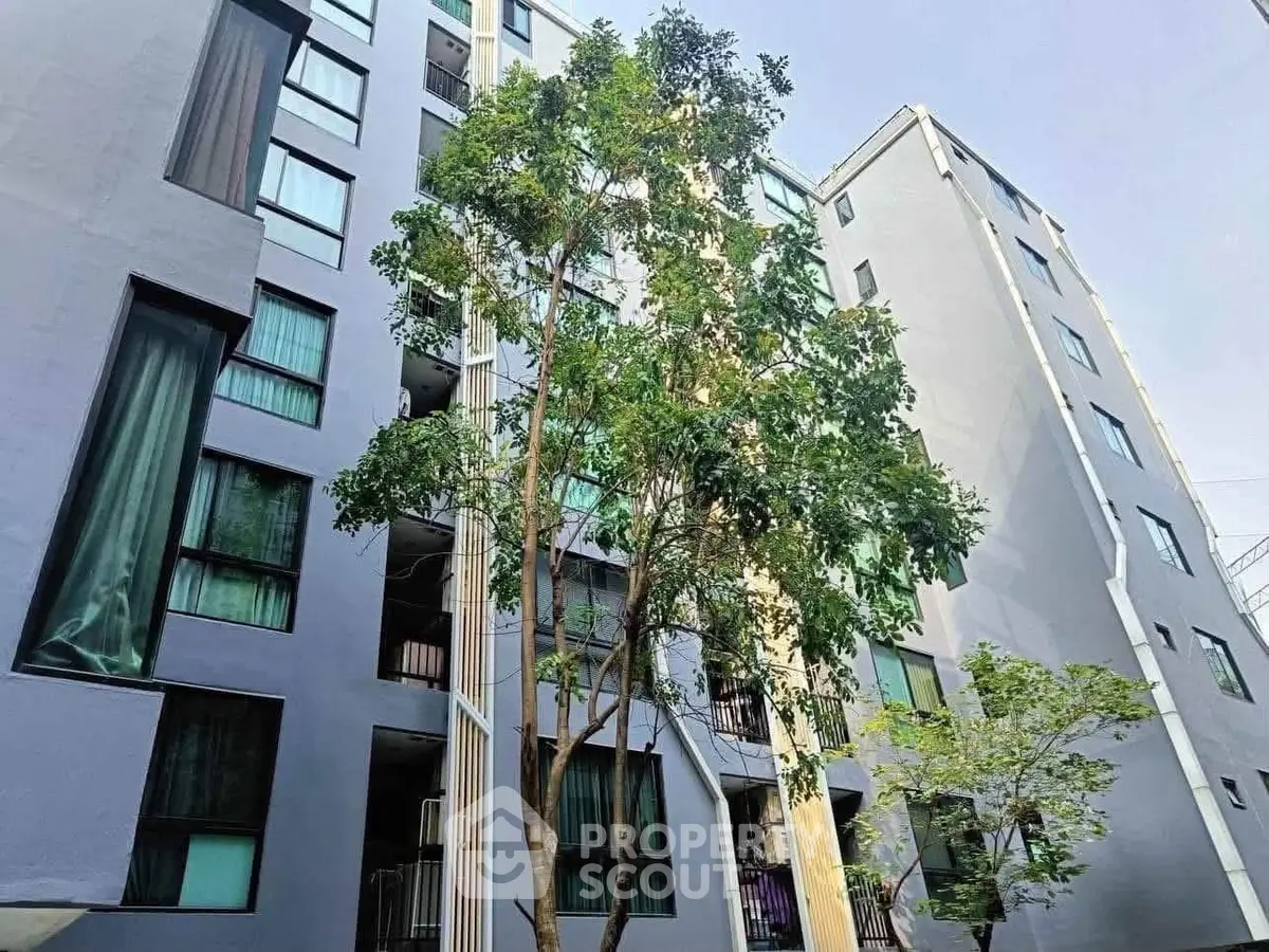 Modern apartment building exterior with lush greenery and tall windows.