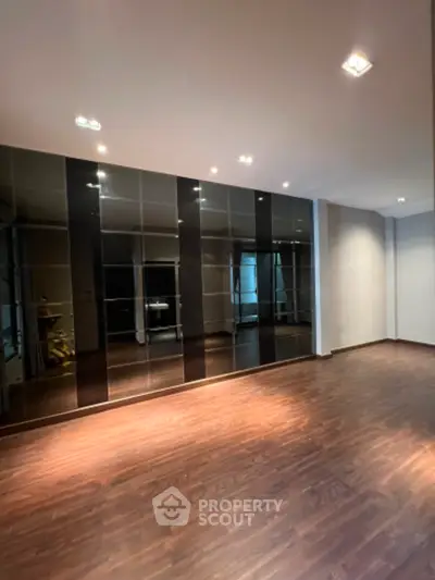 Spacious and modern living room with glossy hardwood floors and a full wall of mirrored closets reflecting ambient lighting.