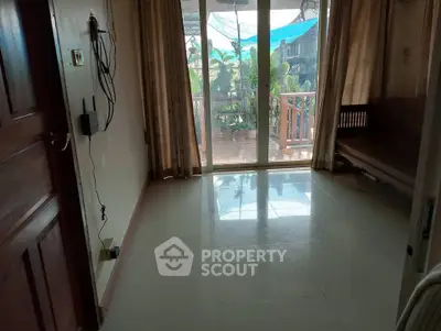 Spacious living room with large windows leading to a balcony, offering a serene garden view.