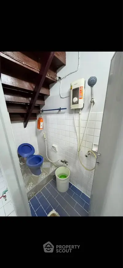 Compact bathroom with blue tiles and water heater under wooden stairs