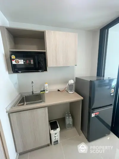 Compact modern kitchen with microwave, fridge, and sink in a stylish apartment.