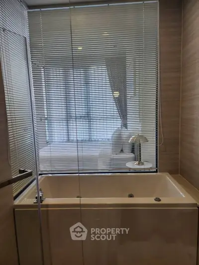 Luxurious bathroom with modern bathtub and glass partition, offering a glimpse of the stylish bedroom.