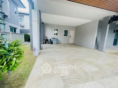 Spacious modern home entrance with covered parking and lush greenery.