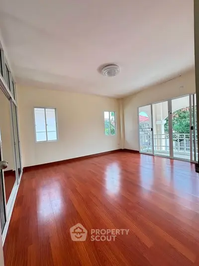 Spacious empty room with wooden flooring and large windows offering natural light.