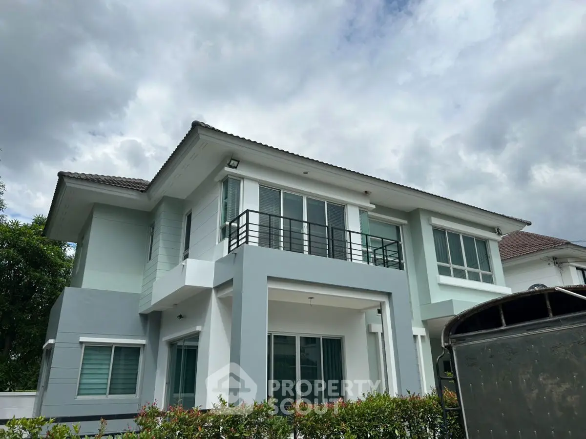 Modern two-story house with large windows and balcony under cloudy sky.