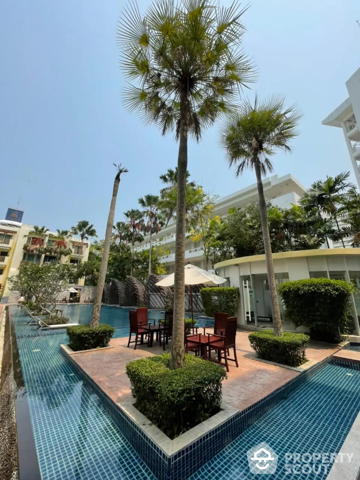 Luxurious outdoor pool area with palm trees and seating in a modern residential complex.