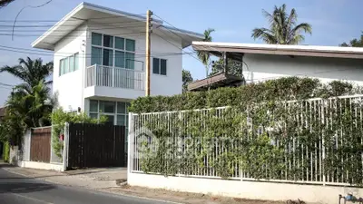 Charming two-story home with a lush green hedge fence, offering privacy and a serene living environment in a tropical setting.