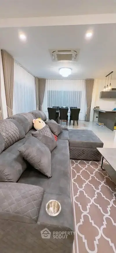Spacious living room with elegant decor and dining area, featuring plush gray sofa and modern lighting.