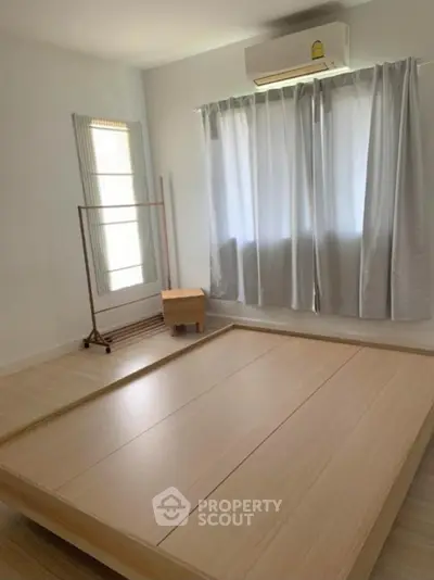 Minimalist bedroom with wooden floor and bed frame, featuring natural light and air conditioning.