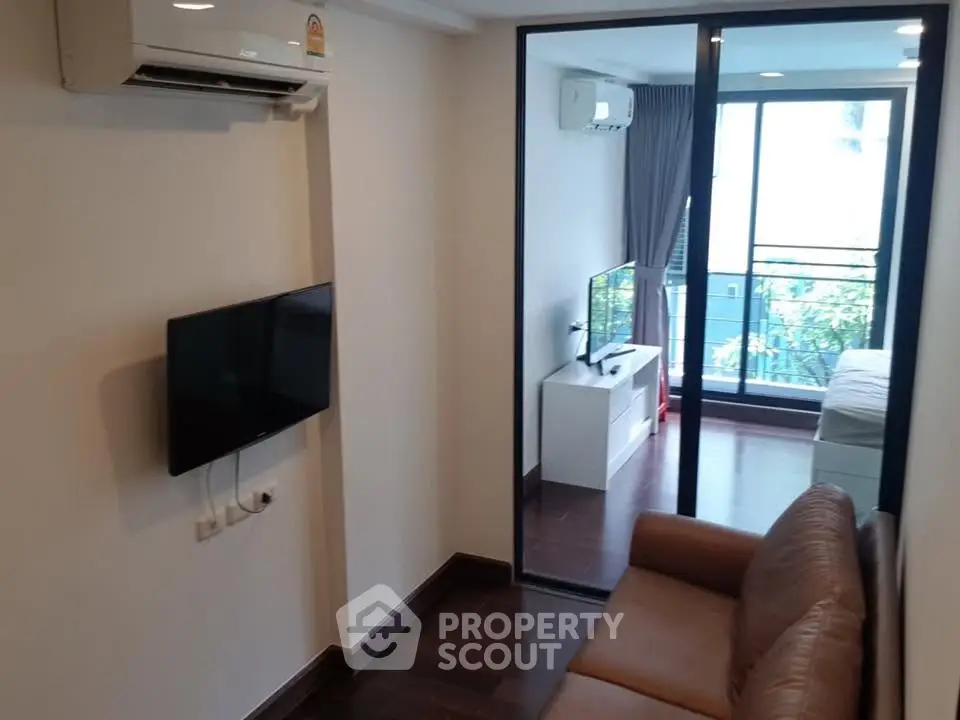 Modern apartment living room with air conditioning and TV, leading to a bedroom with balcony view.