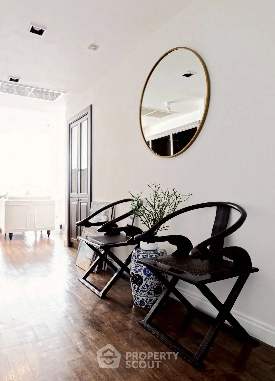 Elegant hallway with wooden chairs and decorative vase under a round mirror