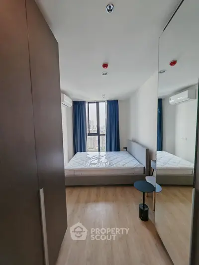 Modern bedroom with large window and city view, featuring sleek furniture and wooden flooring.