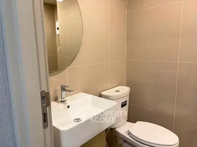 Modern bathroom with sleek fixtures and neutral tiles, featuring a round mirror and compact design.