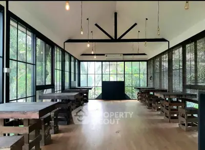 Spacious modern room with large windows and wooden tables, perfect for versatile use.