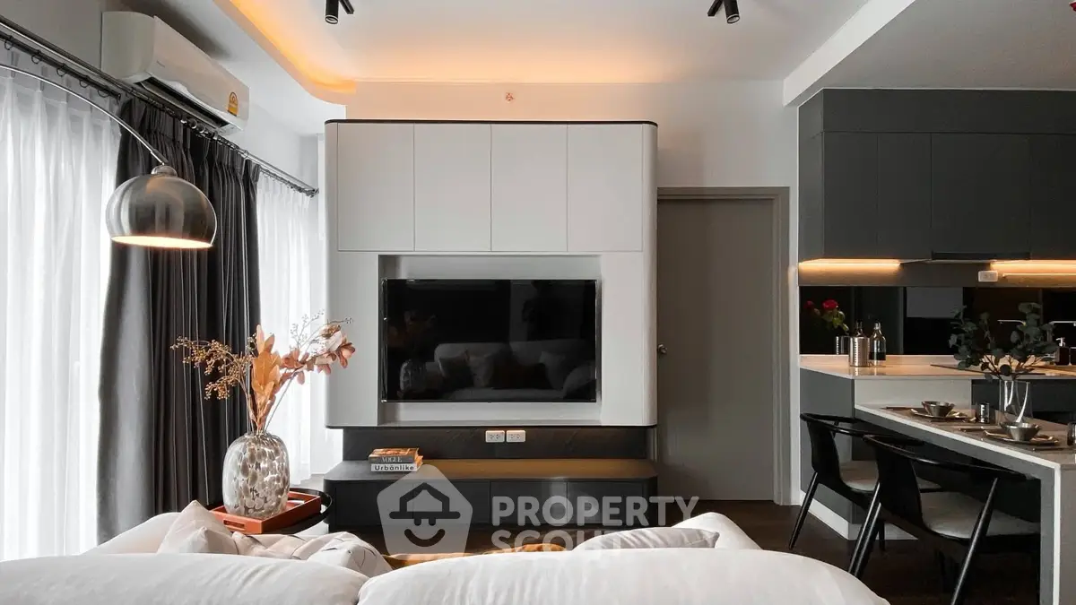 Modern living room with sleek design, featuring a wall-mounted TV, stylish lighting, and open kitchen layout.