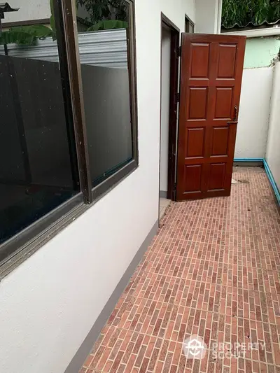 Charming home entrance featuring a classic wooden door and large windows, set against a clean, white facade with a terracotta-tiled pathway.