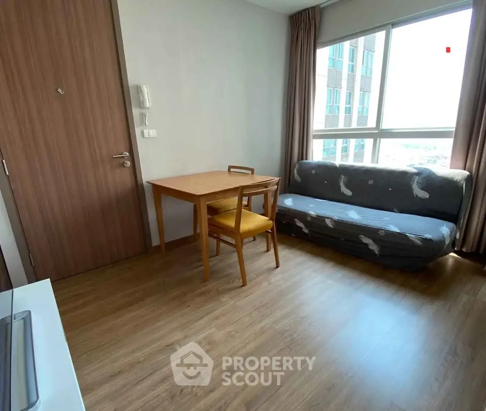 Cozy living room with wooden flooring, compact dining set, and large window offering natural light.