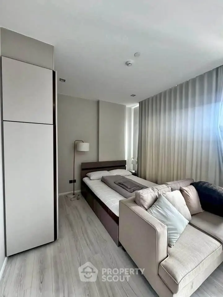 Modern bedroom with sleek design and cozy sofa, featuring floor-to-ceiling curtains and minimalist decor.