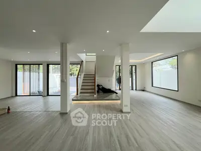 Spacious modern living room with open layout and elegant staircase, featuring large windows for natural light.