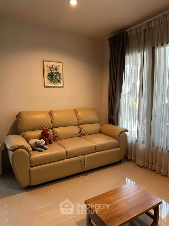 Cozy living room with beige leather sofa and natural light from large window, perfect for relaxation.