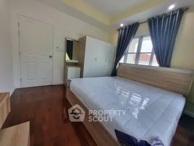 Spacious bedroom with wooden flooring and modern furniture, featuring a large window with elegant curtains.