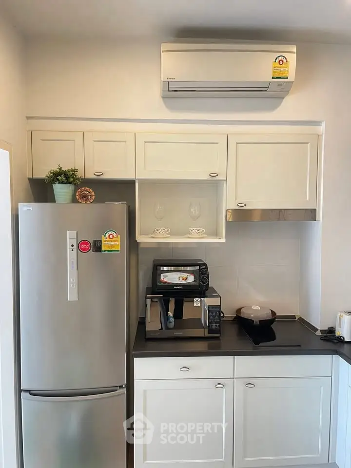 Modern kitchen with sleek appliances and white cabinetry, featuring a stainless steel fridge and air conditioning unit.