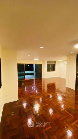 Spacious empty living room with polished wooden floors and large windows.