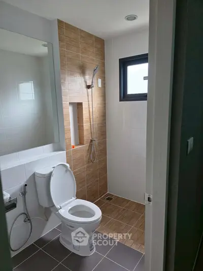Modern bathroom with sleek shower and toilet, featuring stylish tile design and natural light.