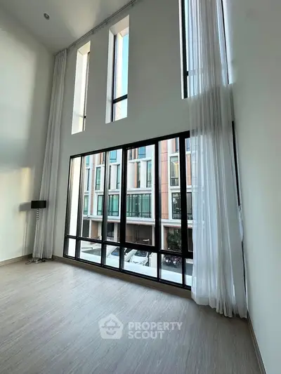 Spacious modern living room with floor-to-ceiling windows and elegant curtains, offering a stunning view.