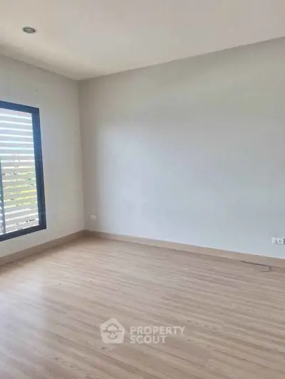 Spacious empty room with wooden flooring and large window, perfect for customization.