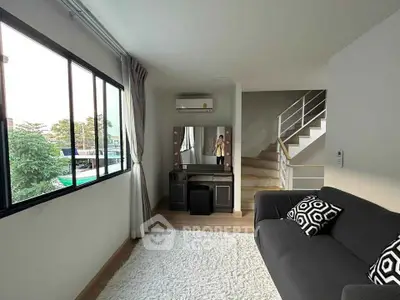 Modern living room with large window, stylish sofa, and staircase in a bright, airy space.