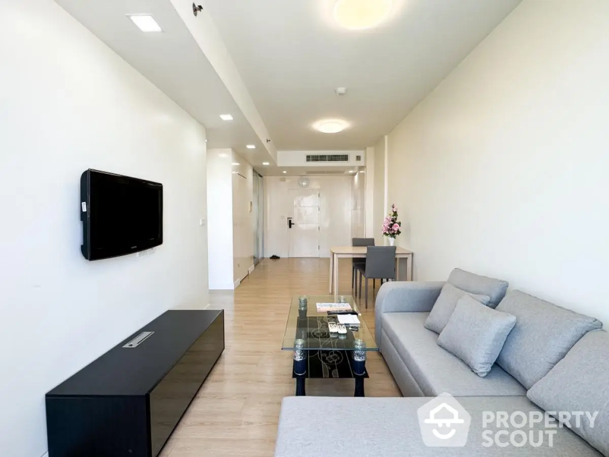 Spacious modern living room with sleek furniture and wall-mounted TV in a bright apartment.