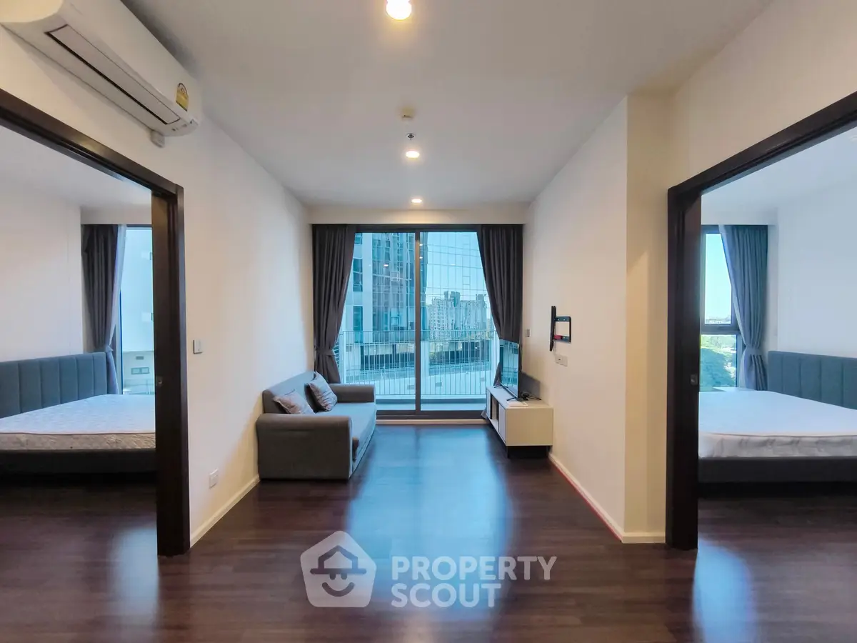 Modern living room with large windows and city view, featuring sleek furniture and hardwood floors.