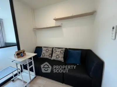 Cozy living room with modern black sofa and decorative cushions, featuring minimalist wall shelves and a compact table.