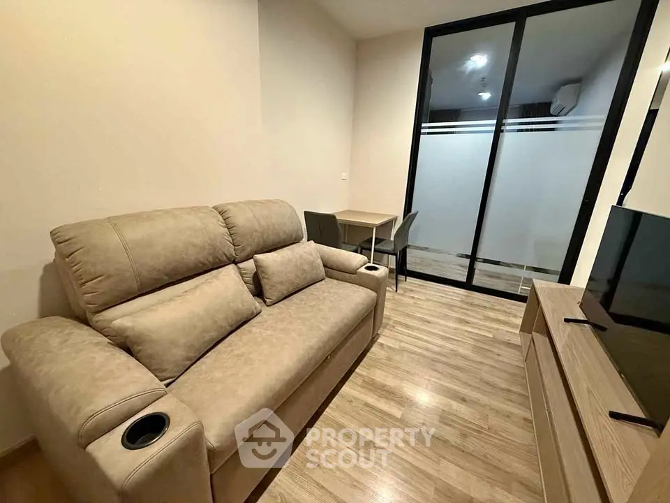 Cozy living room with beige sofa, modern TV stand, and sliding glass doors leading to a balcony.