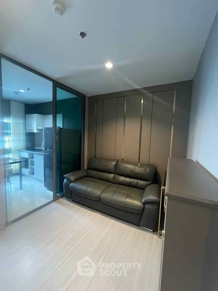 Modern living room with sleek design and glass partition leading to kitchen area.