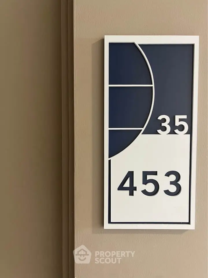Modern apartment number sign with stylish design on beige wall.