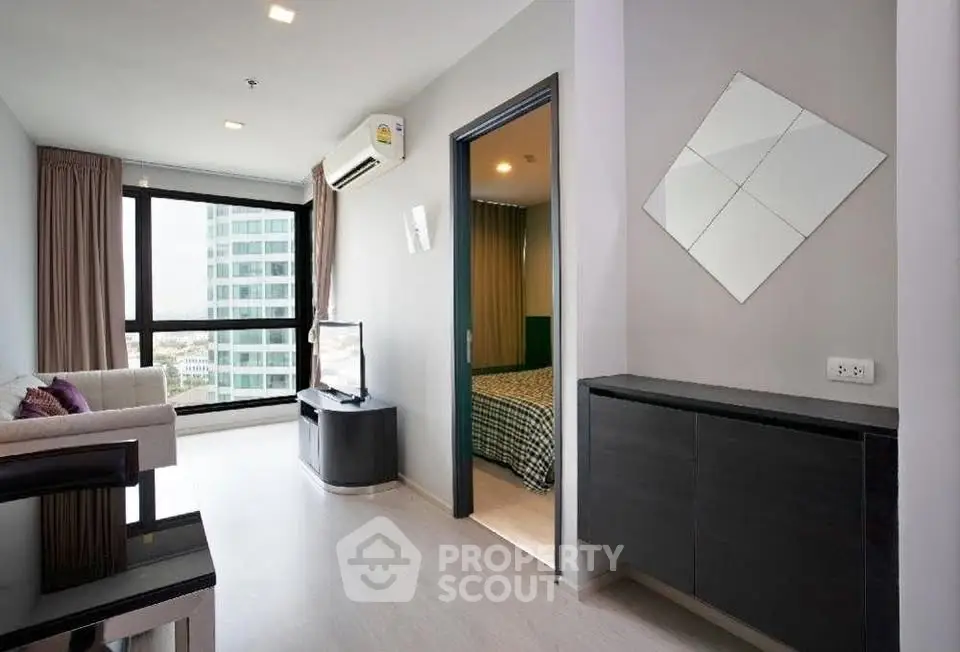 Modern living room with sleek furniture and large window offering city views.